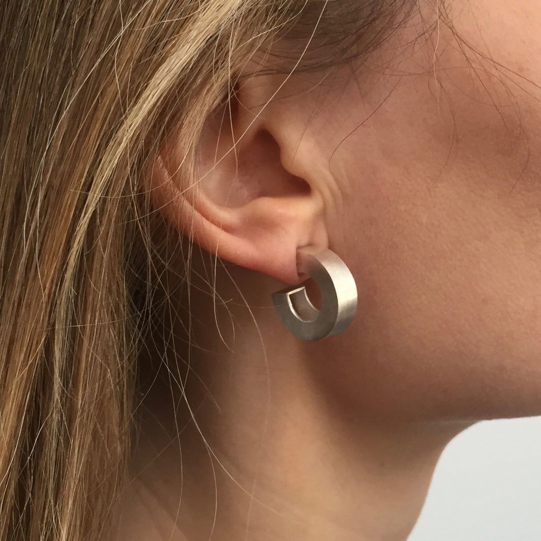 Chunky silver hoop earrings being worn by model.